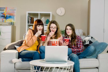 Yemek ve filmler. Evde güzel oda nın kanepesinde otururken film veya spor programı izlerken patlamış mısır yeme üç duygusal güzel kız kardeş.