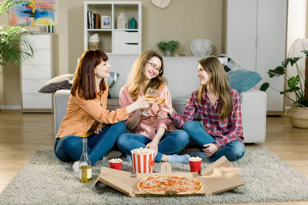 Girls party. Festive occasion. Ladies in casual jeans and shirts. Happy girls clinking glasses with wine, laughing, having fun. Pizza party at home of three female friends