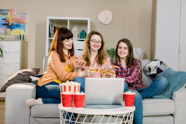 Drie jonge vrouwen kijken naar film op laptop, lachen, drinken wijn en eten smakelijke popcorn thuis — Stockfoto
