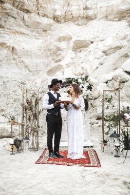 Boho mutlu güzel çift güzel rustik düğün pastası tutan giymek, kanyon açık havada düğün kemer ve süslemeleri arka planda ayakta