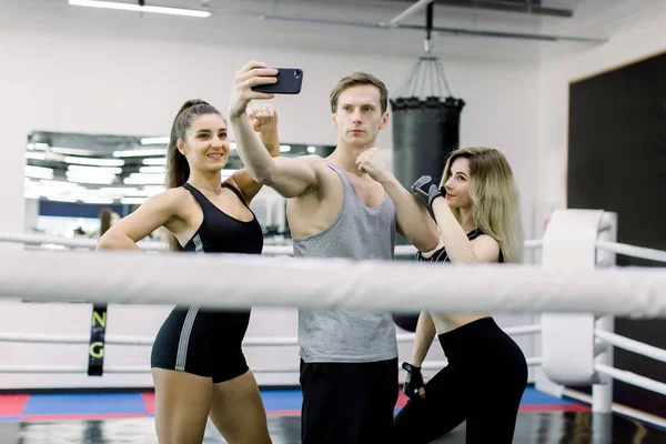 Three professionl boxers and fitness trainers are making selfie while standing in the middle of boxing ring