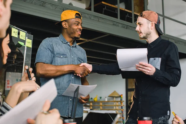 Kreativa afrikanska och kaukasiska unga män skakar hand under arbetsmötet i Office. Team arbete, kontor, IT, frilans — Stockfoto