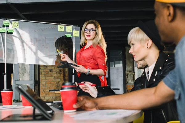 Empresária confiante em camisa vermelha comentando resultados de marketing para colegas em reunião. Freelance, trabalho em equipe — Fotografia de Stock
