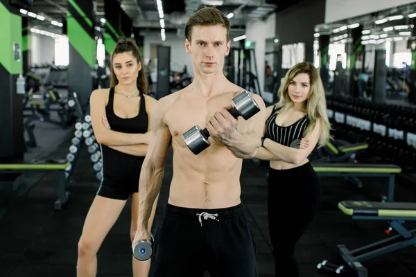 Lifestyle portrait of handsome muscular man with dumbbell in the gym. Young people training in the gym with barbells