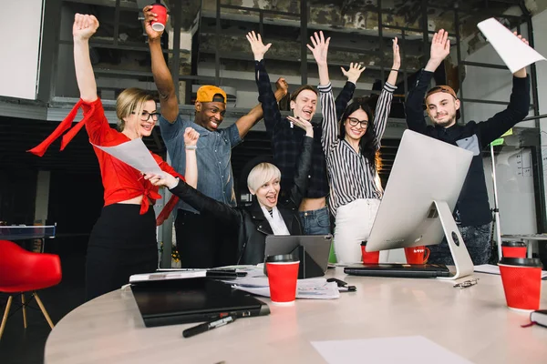 Stora nyheter. Glad leende affärsmän i casual kläder triumferat med armar upp medan du tittar på laptop och dator i moderna kontor — Stockfoto