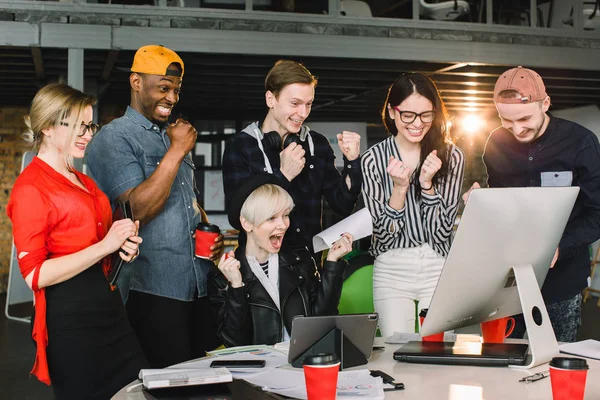 Gyönyörű multietnikus fiatal üzletemberek alkalmi ruhákat használ egy laptop és tabletta, beszél, és mosolyogva munka közben hivatalban — Stock Fotó