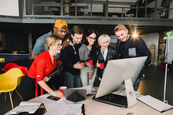 Unga kvinnor och män frilansare eller Det arbetare som använder laptop, titta på sitt arbete. Inomhusporträtt av multietniska kontorsarbetare som dricker kaffe och pratar — Stockfoto