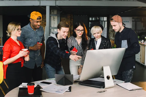 Unga kvinnor och män frilansare eller Det arbetare som använder laptop, titta på sitt arbete. Inomhusporträtt av multietniska kontorsarbetare som dricker kaffe och pratar — Stockfoto