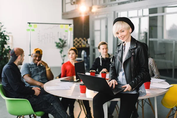 Ung affärskvinna i vardagskläder som arbetar vid skrivbordet med bärbar dator. Olika grupper av affärsmän möts på moderna kontor. — Stockfoto