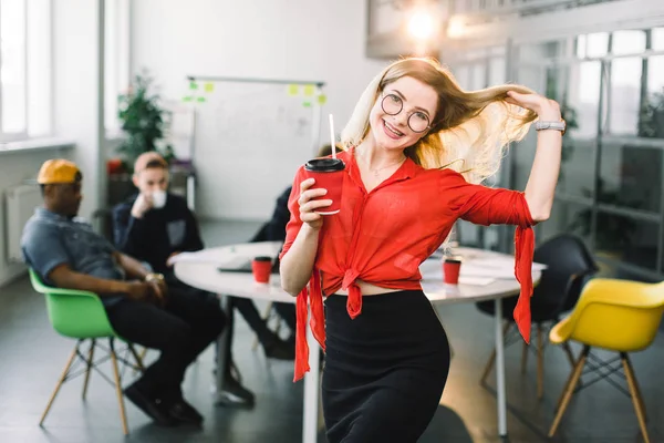 Portrait de jolie femme d'affaires avec une tasse de café travaillant à un grand coworking. Journée de travail ordinaire dans le bureau du loft. Groupe de jeunes gens d'affaires travaillent ensemble avec ordinateur portable, tablette, téléphone intelligent . — Photo