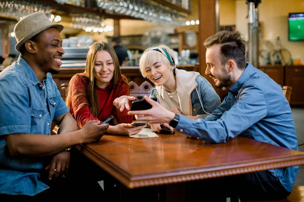 Portrait de jeunes amis joyeux regardant le téléphone intelligent tout en étant assis dans un café. Des gens de race mixte assis à une table dans un restaurant utilisant un téléphone portable . — Photo