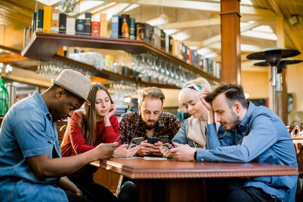 İnsanlar Toplantı İletişim Teknolojisi Dijital Tablet Kavramı. Bir kafe barda oturup akıllı telefonlara bakan beş çok ırklı öğrenciden oluşan bir grup - Genç neşeli arkadaşlar eğleniyor — Stok fotoğraf