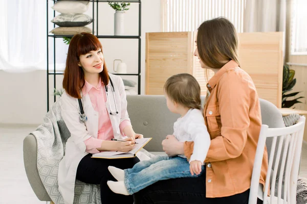 Vriendelijke jonge vrouw pedician arts praat met moeder van kleine baby meisje na onderzoek — Stockfoto
