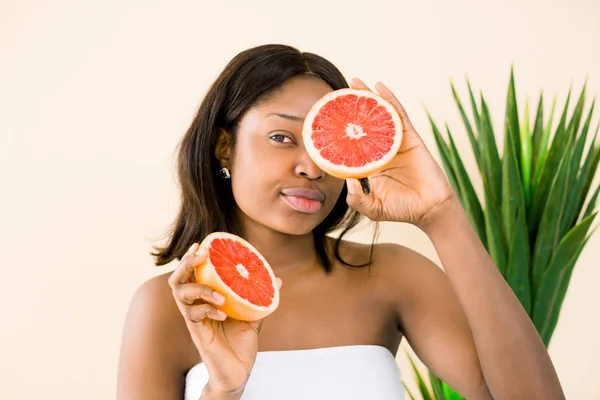 Bájos fiatal afrikai lány gazdaság szelet grapefruit előtt az arcát. Fotó a mosolygó afro-amerikai nő izolált fehér háttér. Beauty bőrápolás koncepció — Stock Fotó