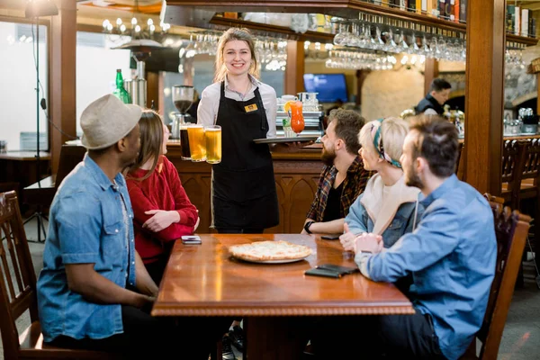 실내 레스토랑에서 젊은 다양한 친구들을 미소 짓고 음료와 맥주를 마시며 미소 짓는 웨이트리스의 초상화. — 스톡 사진