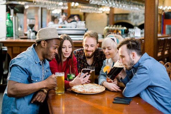 Bir grup neşeli genç arkadaş bir kafede oturuyor, yemek yiyor, içki içiyor. Arkadaşlar selfie çeker ve fotoğraf çeker.. — Stok fotoğraf