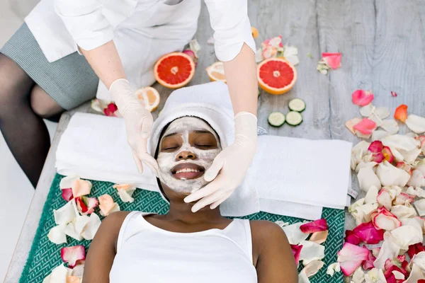 Kozmetológus kenetek kozmetikai maszk az arcon az afrikai nő a Spa szalon — Stock Fotó