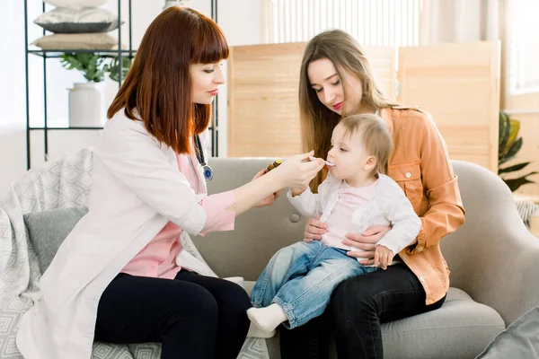 La doctora de casa en bata blanca examina al bebé en casa o en la clínica. Amable médico terapeuta mira da jarabe para la tos — Foto de Stock