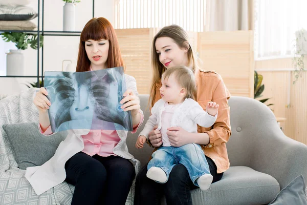 Arts uitleggen borst Xray beeld aan moeder met kleine dochter, zittend op de grijze bank in de kliniek — Stockfoto