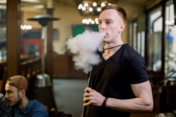 Man smokes hookah in bar. Close-up shot of a stylish adult guy smoking hookah indoor of a cafe.