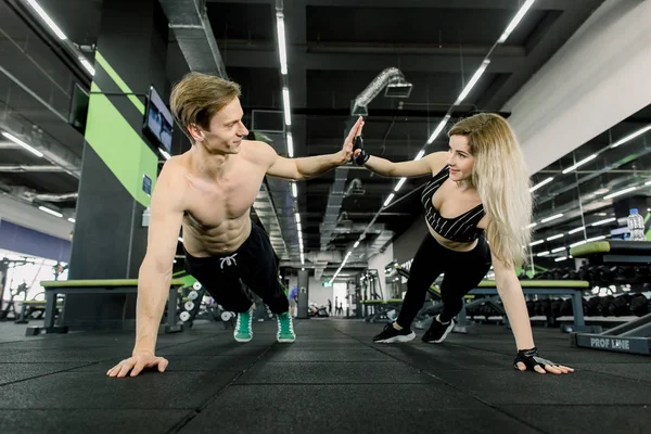 Koppel doet push-ups op training in de sportschool. Jong sportief koppel samen trainen in een fitnessruimte. Planken oefeningen doen terwijl ze elkaar voor één hand houden. — Stockfoto