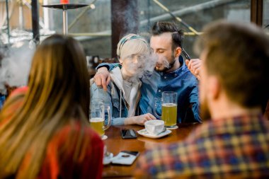 İletişim Kavramıyla Tanışan Kişiler. Bir kafe barda oturup eğlenen bir grup çok ırklı öğrenci. Genç neşeli çift sarılma, öpüşme ve sigara nargile