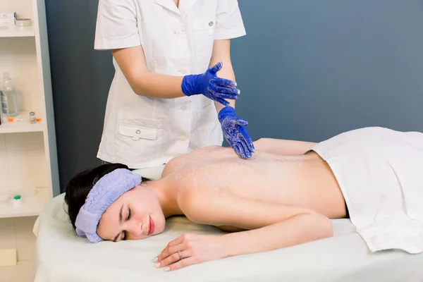 Primo piano di mani massaggiatrici femminili in guanti di gomma blu che danno indietro massaggio ad una giovane bella donna in spa — Foto Stock