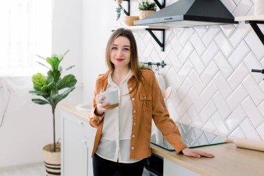 Genç ve mutlu bir kadın sabahları mutfakta kahve içiyor.