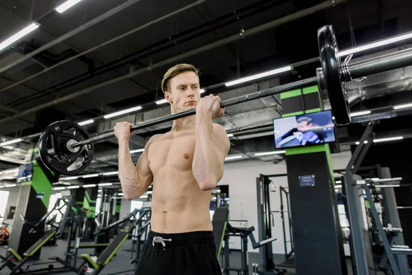 Jonge man flexen spieren met lange halter in de sportschool — Stockfoto