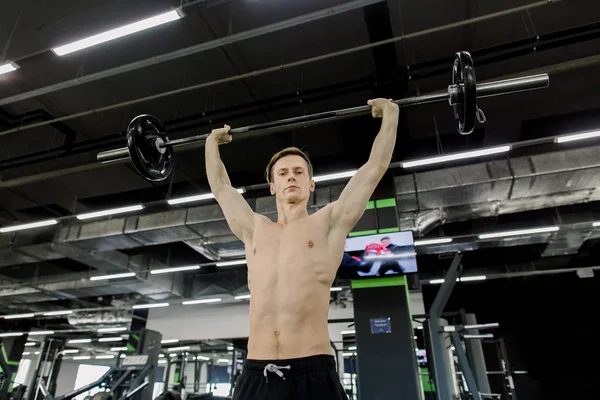 Jonge man flexen spieren met lange halter in de sportschool — Stockfoto