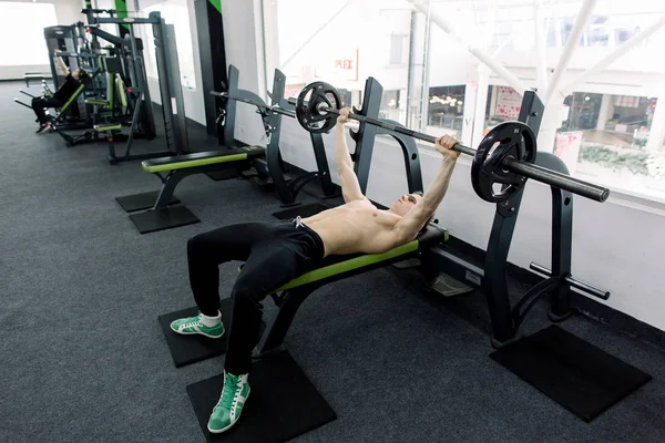 Jonge gespierde blanke man tillen barbell op de Bank in de sportschool. — Stockfoto