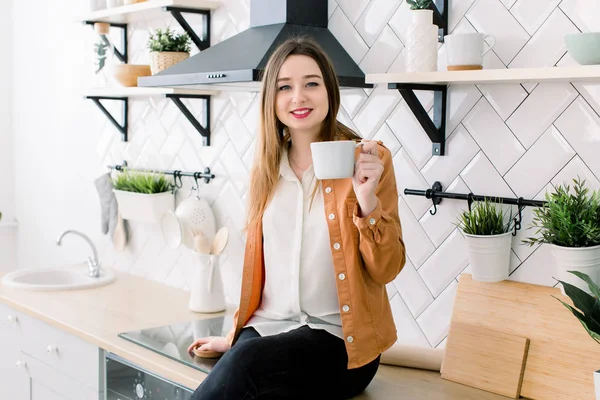 Mujer sosteniendo una taza de café caliente en las manos. Inhalando aroma, disfrutando de la mañana. Cocina luminosa por la mañana . — Foto de Stock