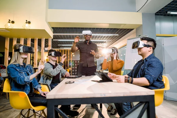 Grupp vänner och deras afrikanska man soffan försöker VR glasögon när du sitter vid bordet i Office. verklig realiteten med folk har nöje tillsammans med bärbara hörlurarna Googles — Stockfoto