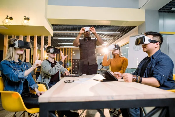 Glada kollegor testar VR-glasögon inomhus. Virtual Reality och bärbara Tech Concept med unga människor att ha kul tillsammans med headset Goggles. — Stockfoto