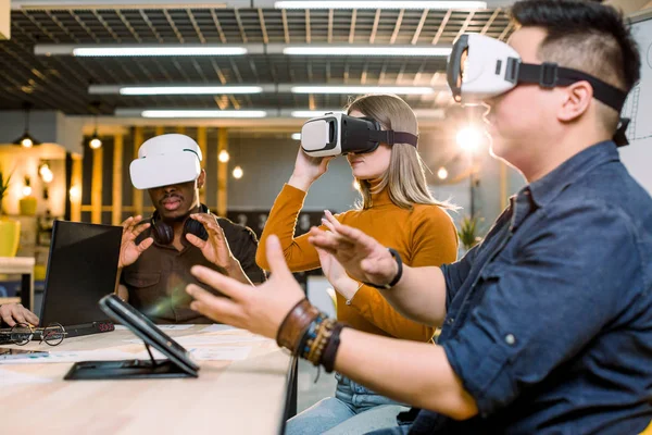 De jeunes amis s'amusent avec un casque de réalité virtuelle assis autour de la table. Des gens heureux utilisant des lunettes modernes vr goggle. Nouvelles tendances et concept technologique — Photo