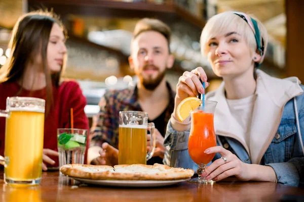 Gülümseyen arkadaşlar pizza yiyor ve meyve suyu içiyor, gülüyor ve restoranda eğleniyor, iş tatilinde loft kafede sehpada oturarak öğle yemeğinin tadını çıkarıyorlar. — Stok fotoğraf