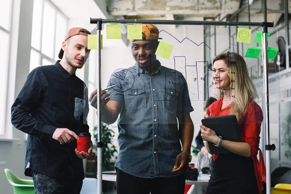 Tre unga affärsfolk som träffas på kontoret och använder post it Notes för att dela idé. Brainstorming-konceptet. Fästis på glasvägg. — Stockfoto