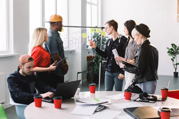 Multietniskt affärsfolk i casual kläder möte på kontoret och använda post it Notes att dela idé. Brainstorming-konceptet. Fästis på glasvägg. — Stockfoto