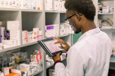 Afro-Amerikan erkek eczacı eczanede dijital tablet notlar yapma, ilaç kalite kontrolü