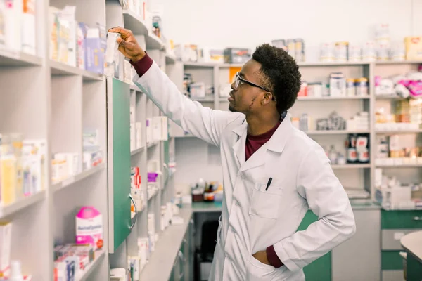 Sebevědomý afroamerický lékárník, který stojí v lékárně a vyhledává drogy na policích v lékárně — Stock fotografie