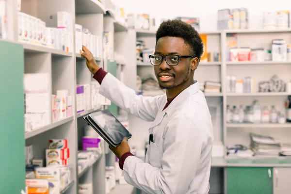 Farmacista afroamericano di sesso maschile che utilizza tablet digitale durante l'inventario in farmacia . Foto Stock Royalty Free