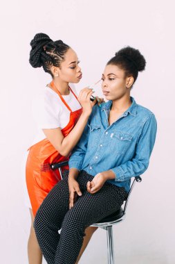 Genç güzel Afro-Amerikan kadın Afrikalı makyaj sanatçısı tarafından profesyonel makyaj uygulayarak. Stüdyo çekimi