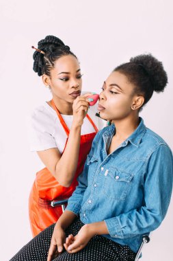 Genç güzel Afro-Amerikan kadın Afrikalı makyaj sanatçısı tarafından profesyonel makyaj uygulayarak. Stüdyo çekimi