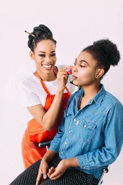 Genç güzel Afro-Amerikan kadın Afrikalı makyaj sanatçısı tarafından profesyonel makyaj uygulayarak. Stüdyo çekimi