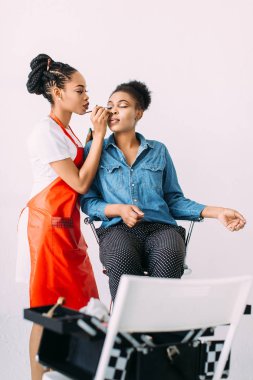 Genç güzel Afro-Amerikan kadın Afrikalı makyaj sanatçısı tarafından profesyonel makyaj uygulayarak. Stüdyo çekimi