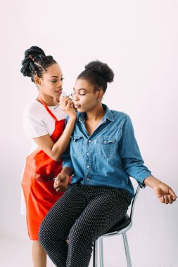 Genç güzel Afro-Amerikan kadın Afrikalı makyaj sanatçısı tarafından profesyonel makyaj uygulayarak. Stüdyo çekimi