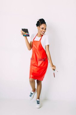 Güzel genç Afro-Amerikan güzellik kadını beyaz izole, fırçalar ve göz farları makyaj seti tutan