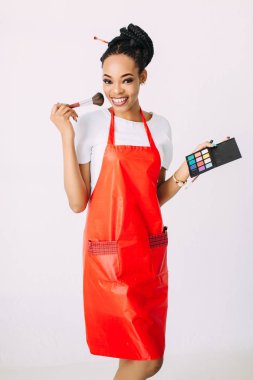 Güzel genç Afro-Amerikan güzellik kadını beyaz izole, fırçalar ve göz farları makyaj seti tutan