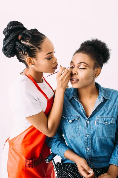 Joven hermosa mujer afroamericana aplicando maquillaje profesional por artista de maquillaje africano. Sesión de estudio —  Fotos de Stock