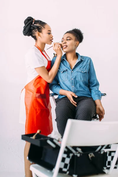 Young beautiful African American woman applying professional make-up by African make-up artist. Studio shoot — Stock Photo, Image